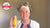 Photo of Maxine Laceby, a white woman with curly grey hair pushed back with a white hairband, she is wearing a white jacket and white necklace and holding up a bottle of Maxerum with a CEW Awards logo superimposed to the top left of the image