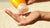 Photo showing a close up shot of a hand as another hand squeezes SPF from an orange bottle into the palm