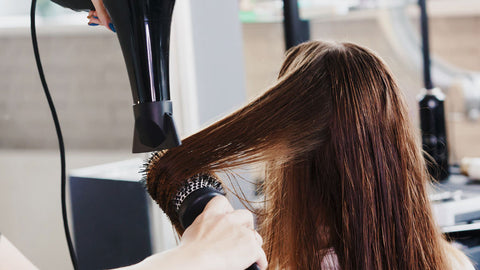 Photo showing a woman with long brunette hair having her hair blow dried