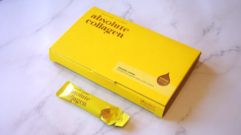 Photo showing a white marble background with a yellow Absolute Collagen box and sachet laying on top of it