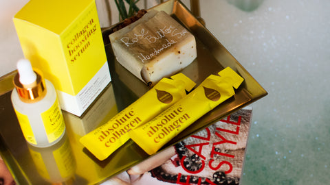 Photo showing two sachets of Absolute Collagen and a bottle of Maxerum on a metallic tray with a bubble bath in the background