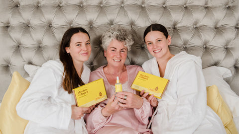 Photo showing Maxine, Margot and Darcy Laceby sat on a bed while wearing dressing gowns and holding up Absolute Collagen boxes and Maxerum bottles