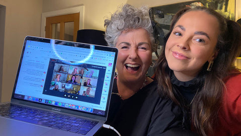 Photo of Maxine and Margot Laceby holding up a laptop with the ladies of Team AC visible on screen, they are all smiling and cheering
