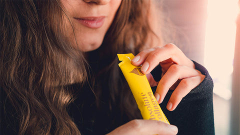 Photo of a white woman with long brown hair holding an Absolute Collagen sachet to her mouth