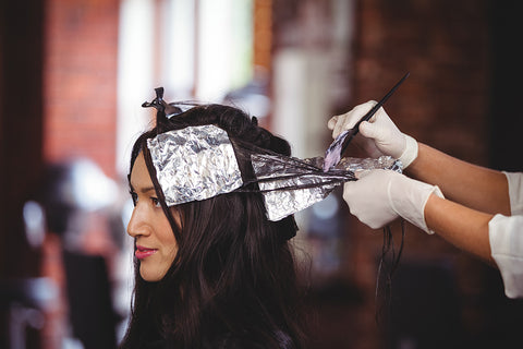 Photo of a woman with long brunette hair having silver foils applied by a hairdresser
