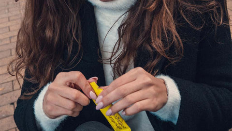 Photo showing a close up of a woman with long brunette hair, she is holding a yellow Absolute Collagen sachet in her hands