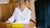 Photo of Eva Proudman, a white woman with short blonde hair, wearing a white lab coat and opening a box of Absolute Collagen, she is sitting at a desk across from a woman with dark brown hair